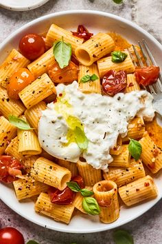 a white bowl filled with pasta, tomatoes and sauce on top of a marble table