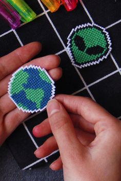 a hand is holding two small pieces of bead art on a black surface with crayons in the background