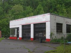 an old abandoned building sits in the middle of a parking lot with trees behind it