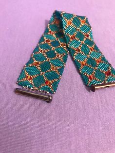 two green and gold patterned hair clips on a purple cloth covered surface with small beads