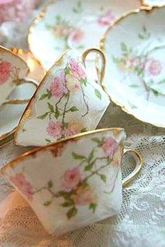 tea cups and saucers with pink flowers on them sitting on a lace tablecloth