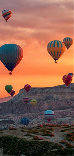 many hot air balloons are flying in the sky at sunset or dawn over mountains and valleys