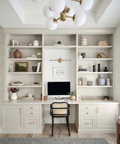 an office with white cabinets and shelves, including a computer on top of a desk