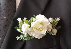 a boutonniere with white flowers and greenery on it's lapel