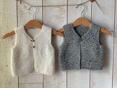 two knit vests hanging on a clothesline against a white wooden wall, one in grey and the other in beige