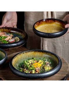 three bowls filled with food on top of a wooden table in front of a person