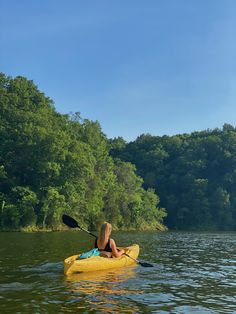 a woman in a yellow kayak paddling on the water with trees behind her