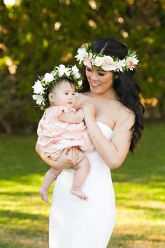 a woman holding a baby in her arms and wearing flowers on top of her head