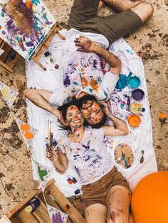 two people are laying on the ground with their faces covered in paint and painting supplies