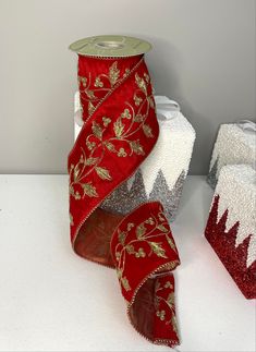 red and silver ribbon with gold leaves on it next to two white boxes filled with christmas decorations