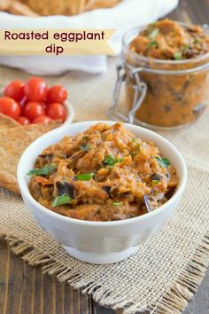 an eggplant dip in a white bowl next to crackers and tomatoes