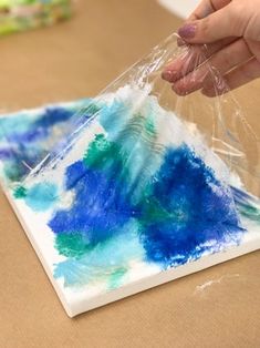 a person is painting on a piece of paper with blue and green colors in it