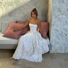 a woman in a white dress sitting on a couch next to pillows and pillow cases