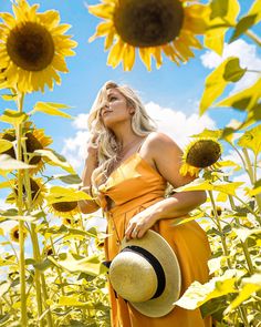 a woman in an orange dress and hat standing in a field of sunflowers