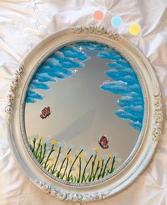 a mirror that is sitting on top of a white sheet with grass and butterflies painted on it