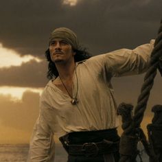 a man in white shirt standing on top of a boat next to the ocean with ropes