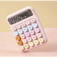 a pink calculator sitting on top of a table next to a yellow wall