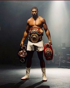 a man standing in the middle of a stage holding two boxing gloves and a belt