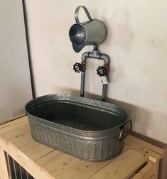 a metal tub sitting on top of a wooden table next to a wall mounted faucet