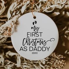 a white ornament hanging from a tree with the words, my first christmas as daddy