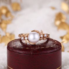 a white pearl ring sitting on top of a wooden box with gold leaves around it