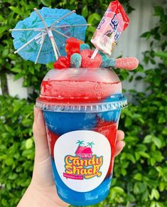 a person holding up a cup with candy shack on it in front of some bushes