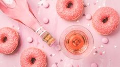 pink donuts with sprinkles next to a glass of wine and spoon