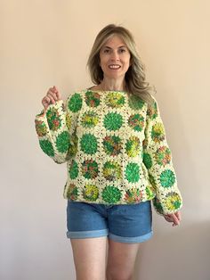 a woman standing in front of a wall wearing shorts and a crocheted sweater