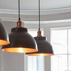 three pendant lights hanging from a ceiling in a room with white walls and round windows