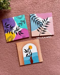 three square paintings with flowers on them sitting on a pink carpet next to a plant