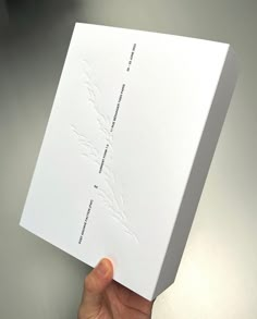 a person holding up a white box on top of a gray surface with writing on it