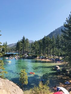 people are swimming in the clear blue water near trees and rocks on a sunny day