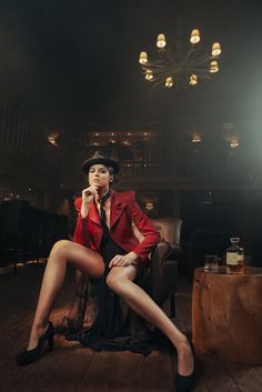 a woman in a red jacket and black dress sitting on a chair with her legs crossed