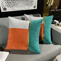 two orange and green pillows sitting on top of a gray couch next to a lamp