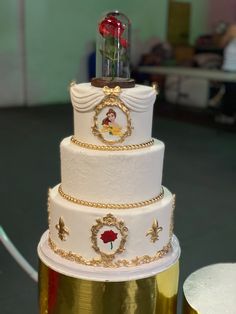 a three tiered white cake with gold trimmings and a red rose on top