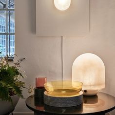 a table topped with a yellow bowl next to a white lamp and potted plant