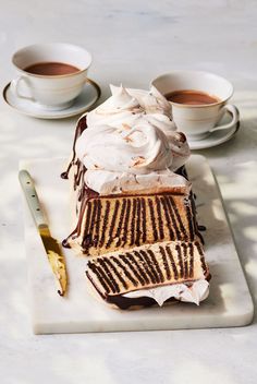 a piece of cake sitting on top of a white plate next to two cups of coffee