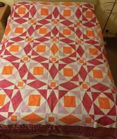 a bed with an orange and pink quilt on it