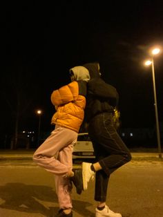 two people standing in the street at night with their arms around each other and one person holding his head