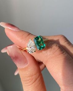 a woman's hand holding an emerald and diamond ring