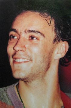 a close up of a person wearing a tie and smiling at the camera with his hair pulled back