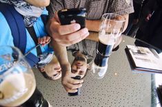 several people sitting at a table looking at their cell phones while drinking beer and talking to each other