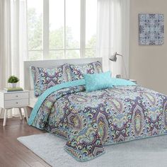 a bed with blue and green comforters in a room next to a white rug