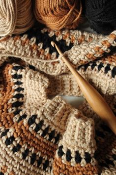 a crocheted blanket with yarn and a wooden knitting needle