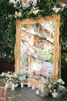 a large mirror sitting on top of a wooden floor next to flowers and candles in vases