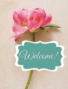 a pink flower sitting on top of a wooden table next to a sign that says welcome