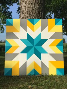 a large quilt sitting next to a tree in the grass with blue, yellow and gray squares on it