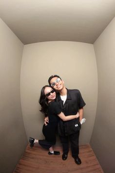 a man and woman pose for a photo in the corner of a room with wood flooring