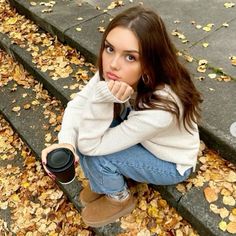 a young woman sitting on the steps with her hand under her chin and holding a coffee cup