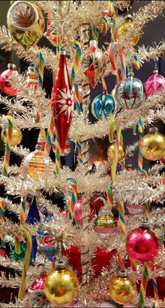 a white christmas tree with ornaments hanging from it's sides and colorful ribbons on the bottom